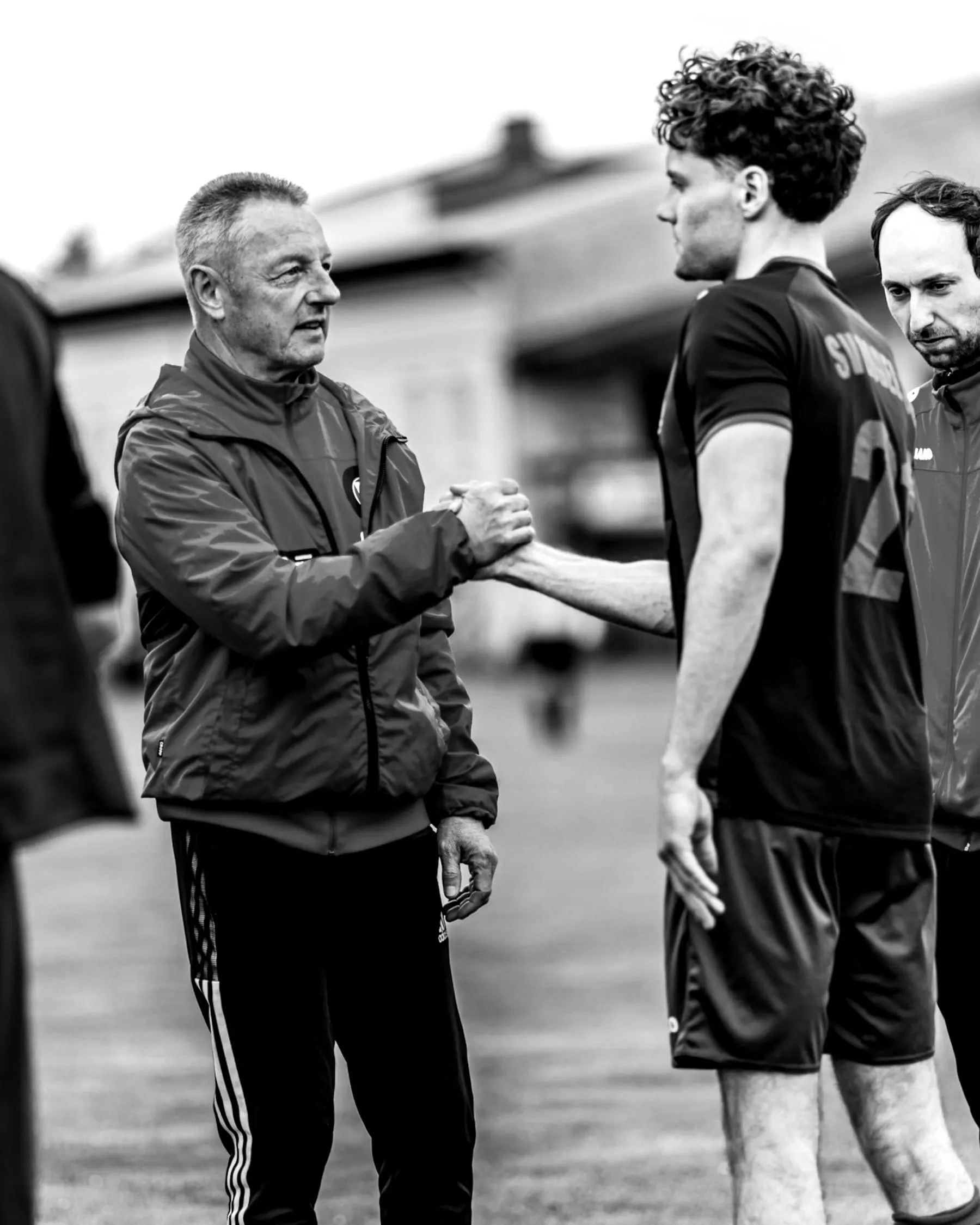 Trainer in roter Jacke und Spieler reichen sich die Hand.