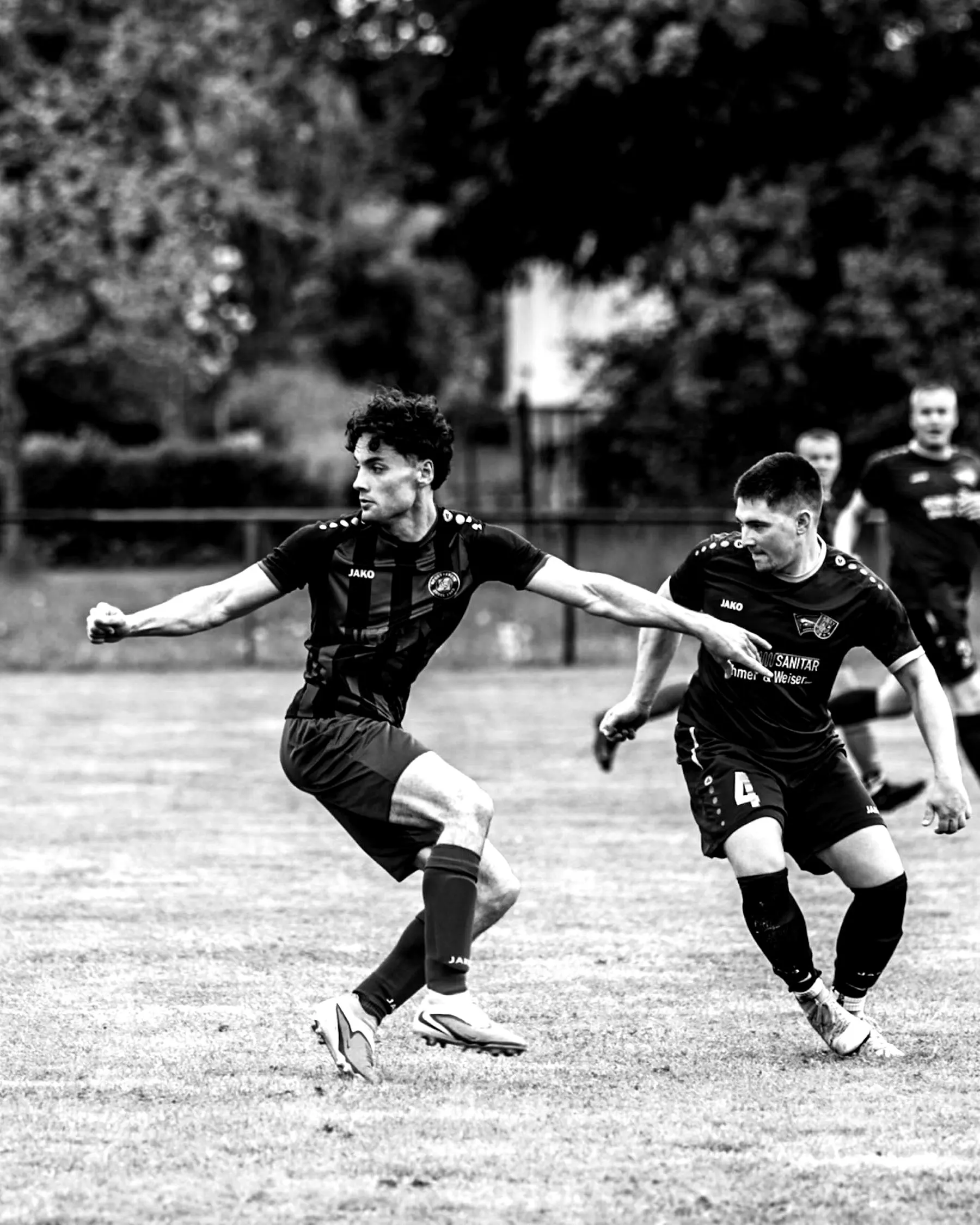 Spieler in Schwarz holt zum Schuss aus, ein Gegner grätscht.