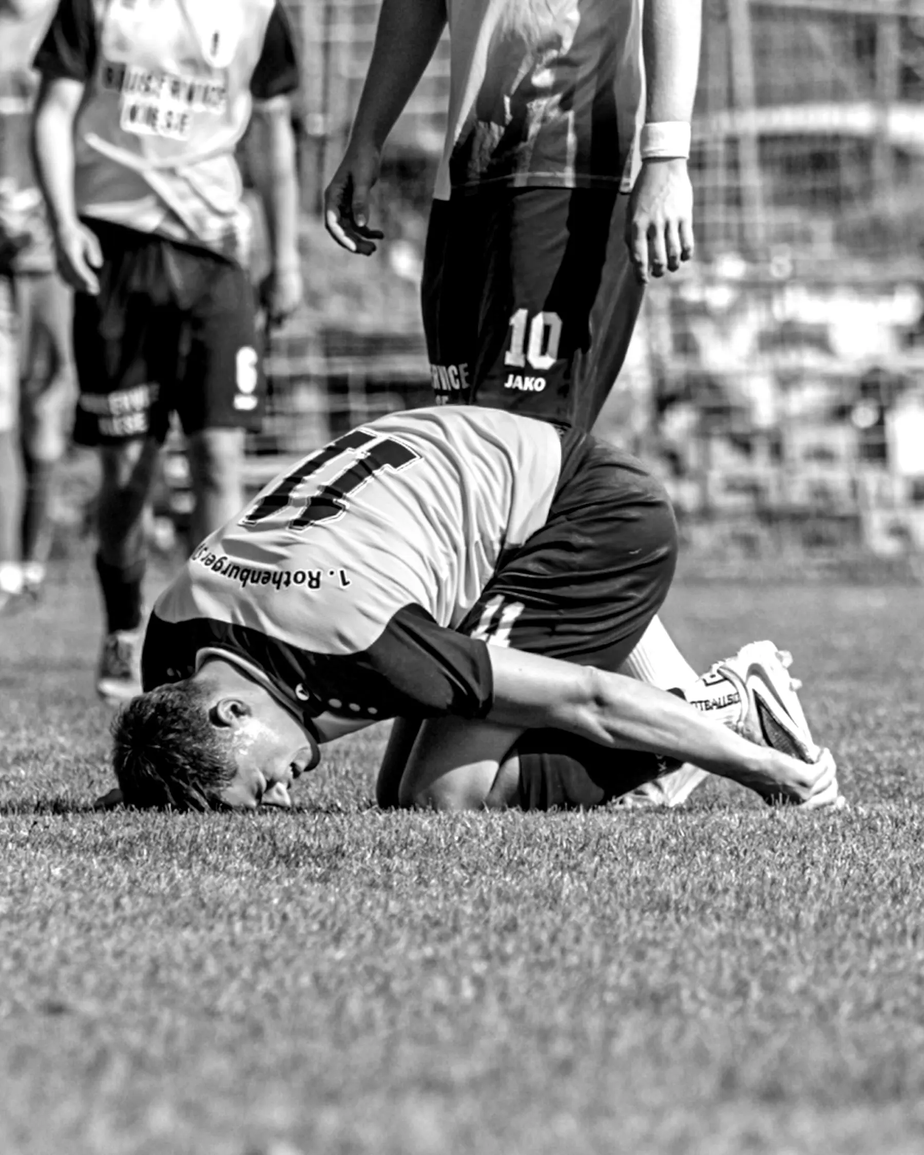 Spieler in Gelb kniet erschöpft mit dem Gesicht am Rasen.