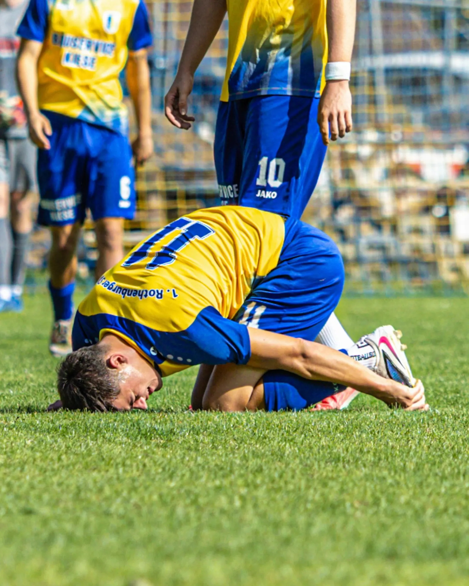 Spieler in Gelb kniet erschöpft mit dem Gesicht am Rasen.