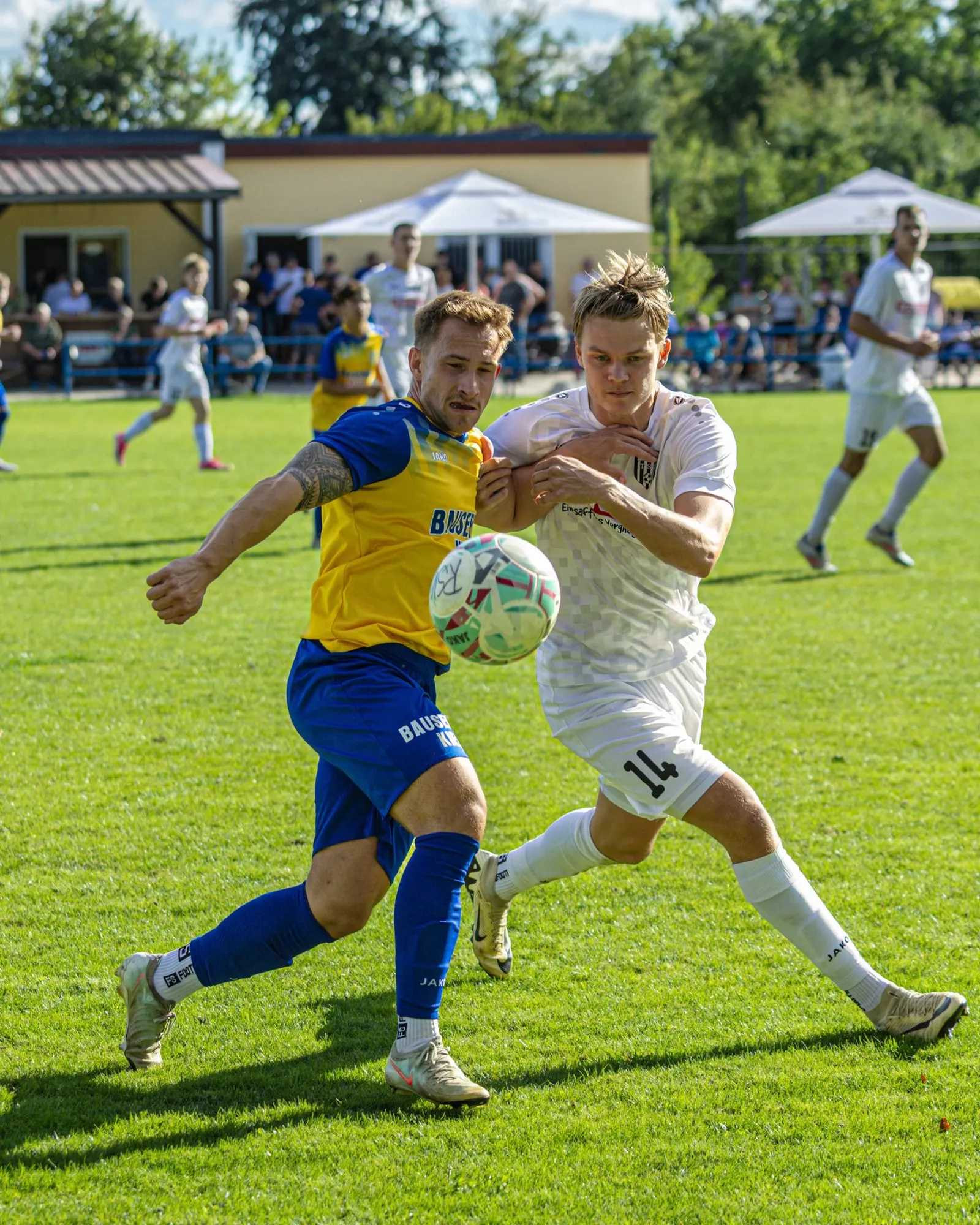 Zweikampf um den Ball, Zuschauer im Hintergrund.