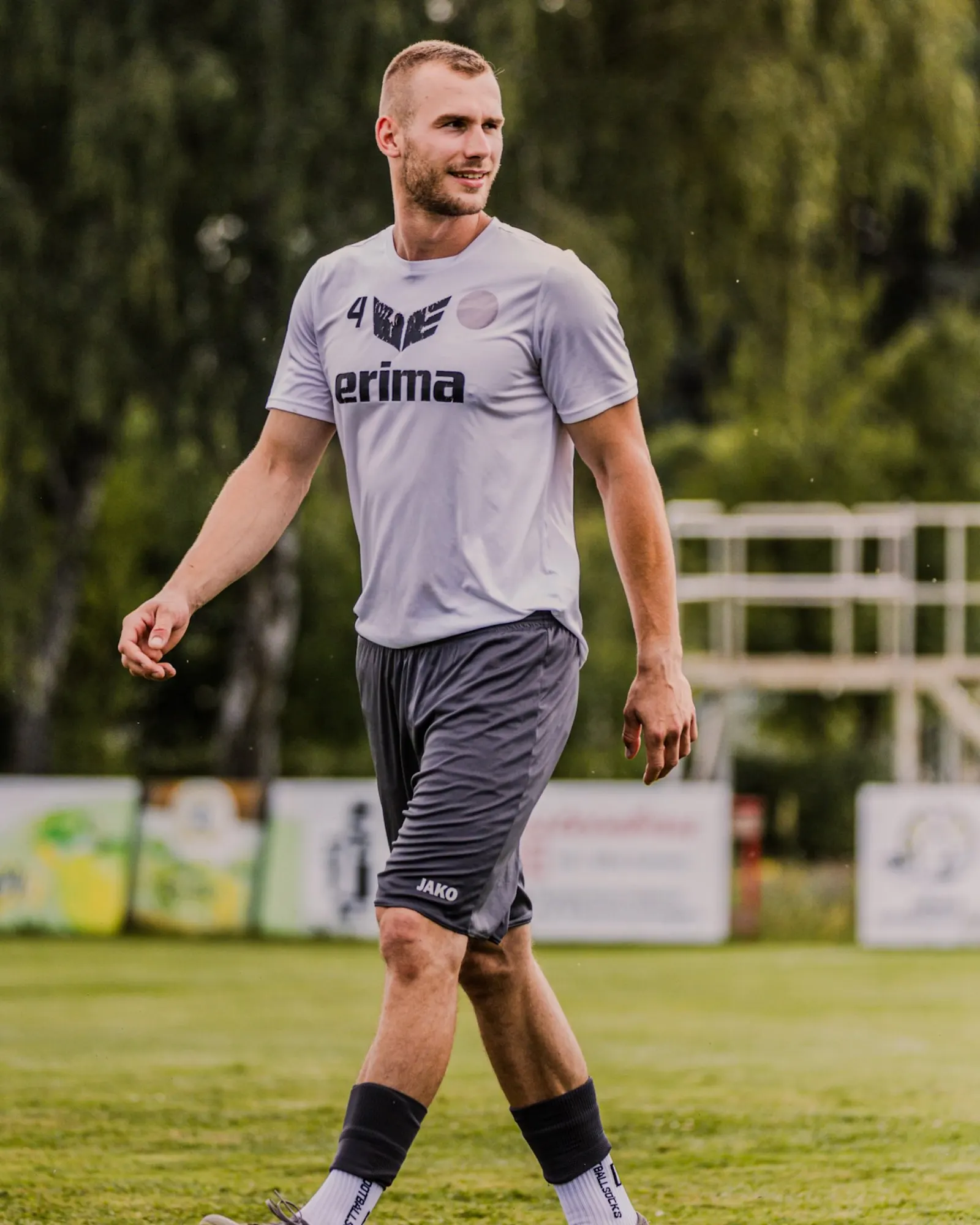 Spieler in hellem Shirt geht über den Rasen, hinter ihm Bandenwerbung.